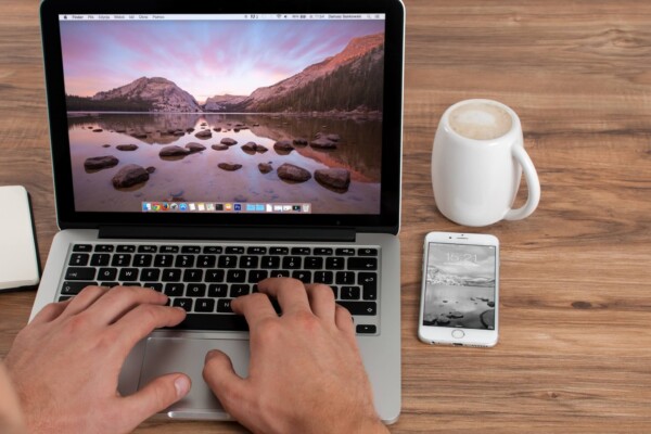 Person on MacBook with iPhone next to them.
