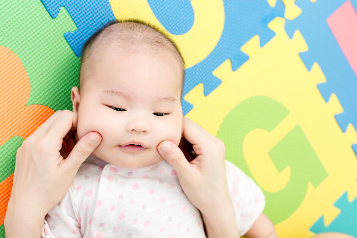 Parent pinch the cheeks a little adorable newborn infant baby girl that lying on the back on colorful eva foam indoors