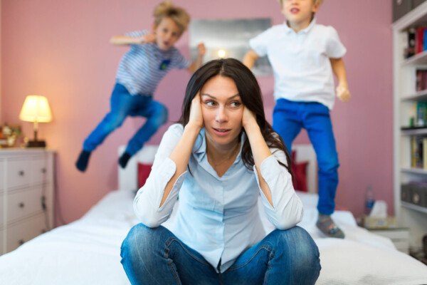 Tired, frustrated mother with children jumping on bed