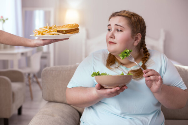 Tasty appealing hamburger enticing obese woman eating salad