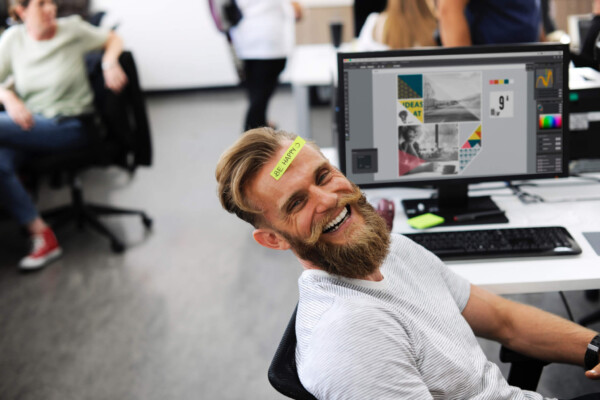 Office employee with "Be Happy" sticker on his head while sitting at desk