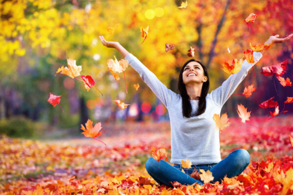 Happy woman throwing autumn leaves in the park