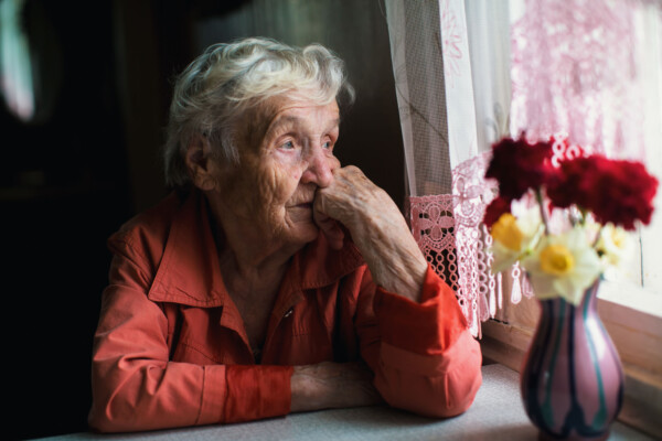 Sad, lonely elderly woman looking out window