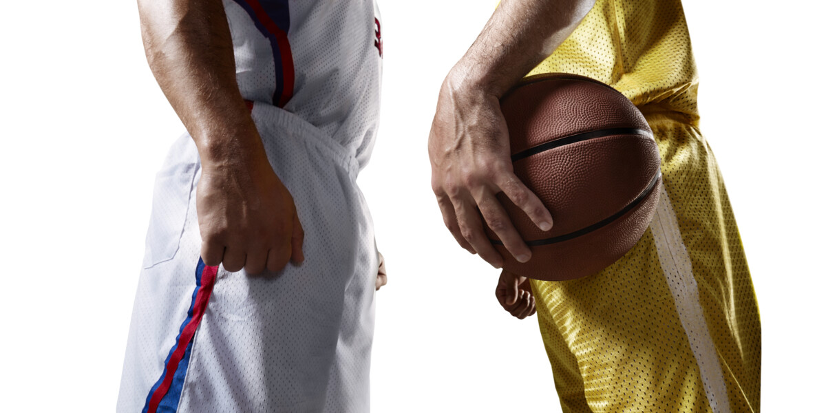 Two basketball players stands face-to-face before the game. Players wears unbranded uniform. One player holds a basketball ball.