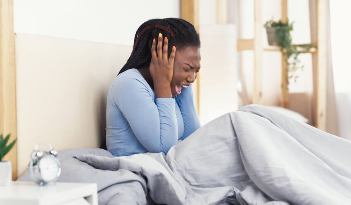 Black Girl Screaming Covering Ears Sitting In Bed At Home