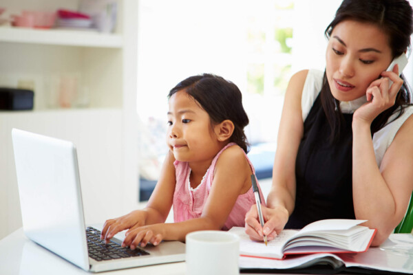 Busy mom working on phone while child plays on computer