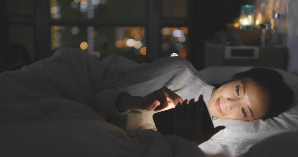 Woman looking at phone in bed, blue light in face