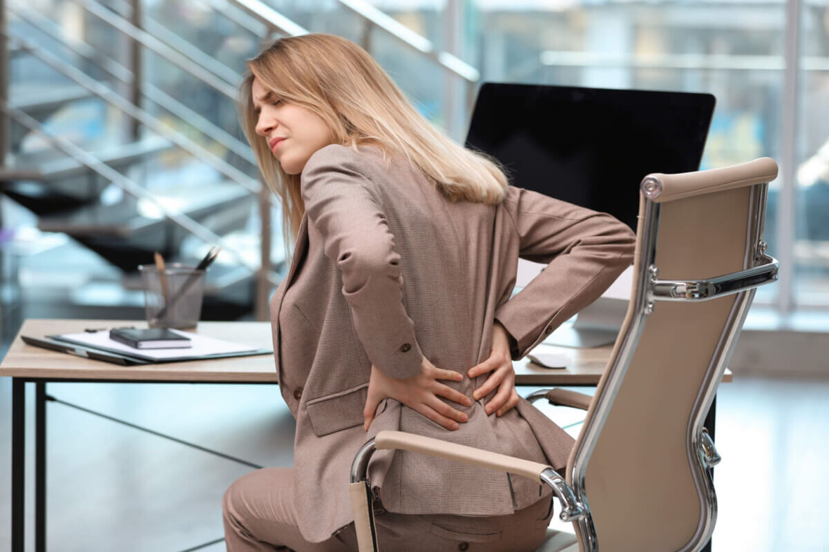 Young woman suffering from back pain in office