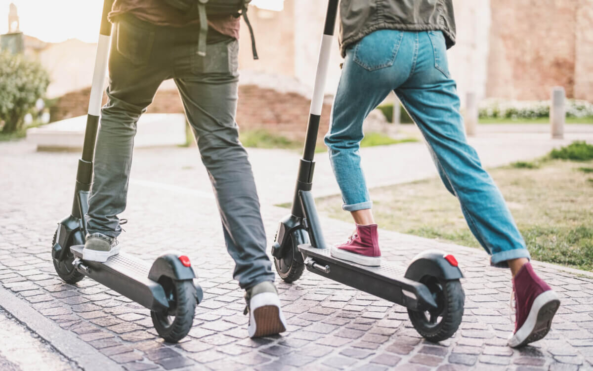 Close up of people couple using electric scooter in city park – Millenial students riding new modern ecological mean of transport – Green eco energy concept with zero emission – Warm sunshine filter
