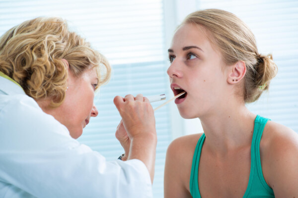 Doctor looking at throat of sick teen girl, possible strep throat