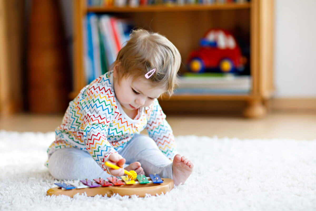 Adorable cute beautiful little baby girl playing with educational wooden music toys at home or nursery. Toddler with colorful xylophon