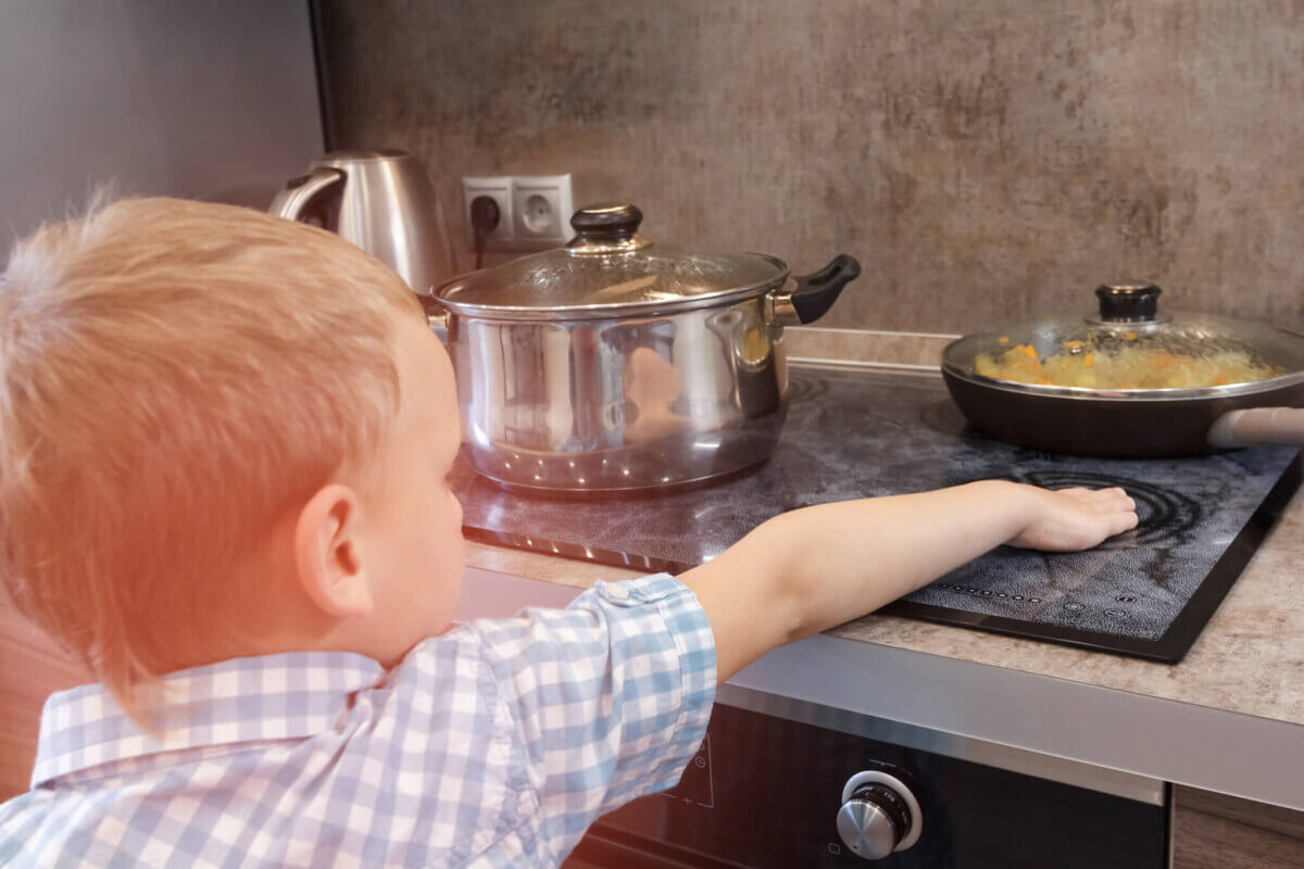 Toddler boy touches hot stove in kitchen. Accident at home with children. Child pulls a hand to a scorching pan