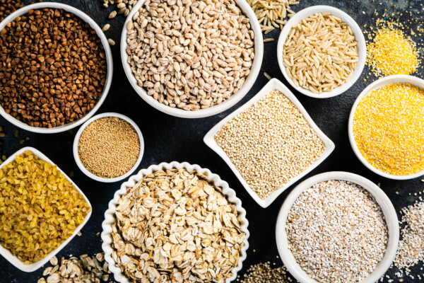 Selection of whole grains in white bowls - rice, oats, buckwheat, bulgur, porridge, barley, quinoa, amaranth