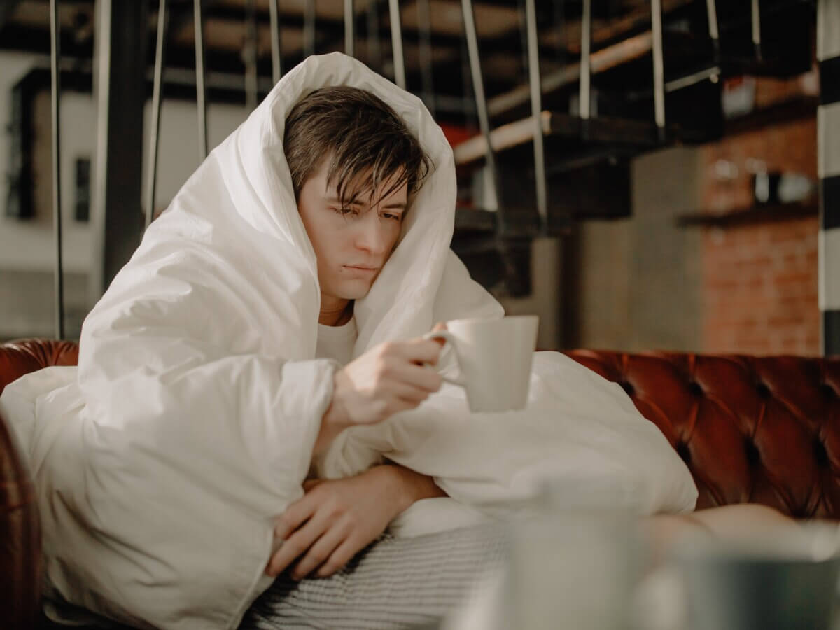 Sick man covering himself with blanket, drinking tea