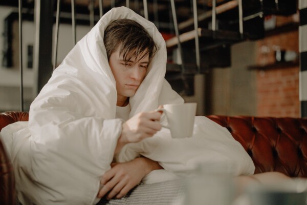 Sick man covering himself with blanket, drinking tea