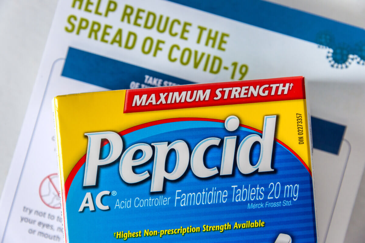 Pepcid AC (Famotidine) antacid medicine in front of a Covid-19 prevention document