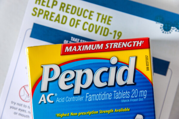 Pepcid AC (Famotidine) antacid medicine in front of a Covid-19 prevention document