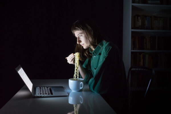 Woman eating noodles as late night dinner in front of computer in dark room