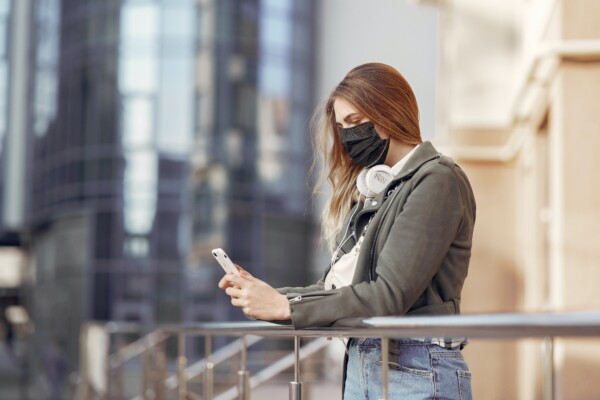 Woman wearing face mask while texting on phone during COVID-19 / coronavirus outbreak