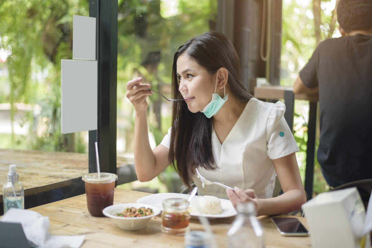 Woman with face mask while eating at restaurant during coronavirus outbreak