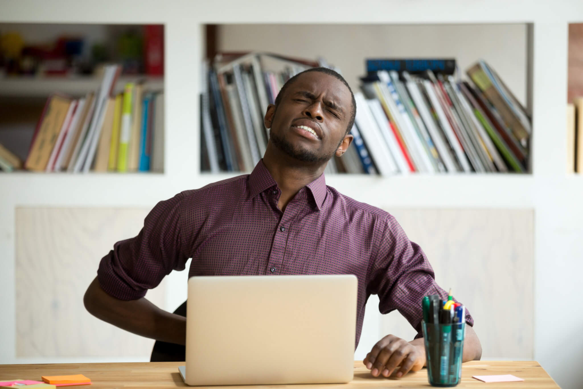 Man bothered by back pain while working at desk, home office