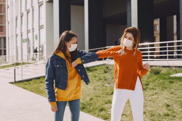 Women in masks elbow-bumping and social distancing during coronavirus pandemic