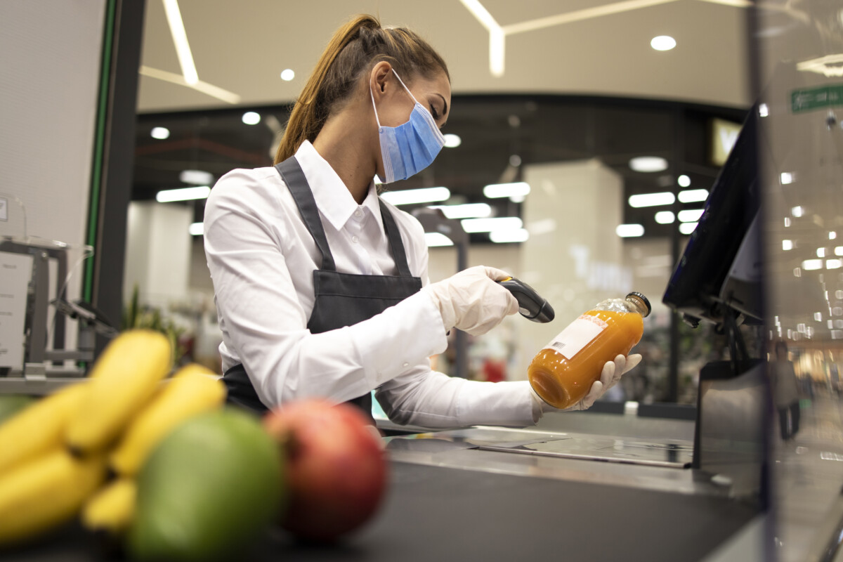 Cashier in supermarket wearing mask and gloves fully protected against corona virus. Working during covid-19 pandemic.