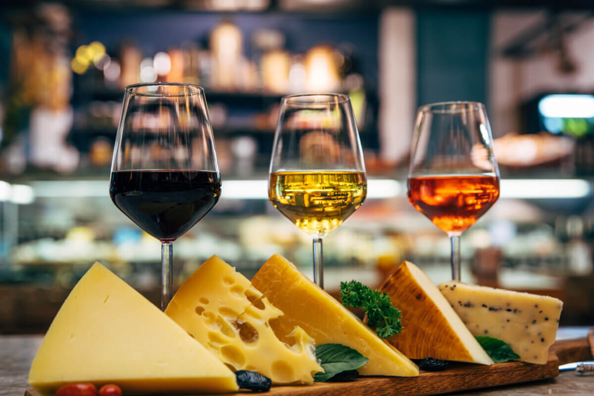 Glasses of Wine and cheese. Assortment or various type of cheese and wine glasses on the table in restaurant. Red, rose and yellow wine or champagne on the table. Winery concept image