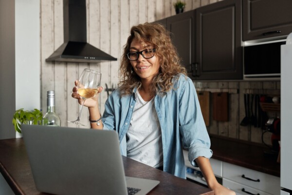 Woman drinking glass of wine on video chat with computer