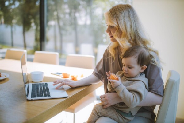Mother holding child on lap while doing work on laptop