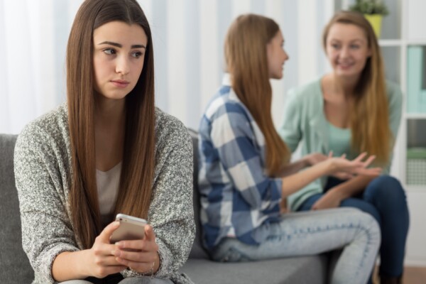 Sad or jealous girl holding phone while friends talk behind her back