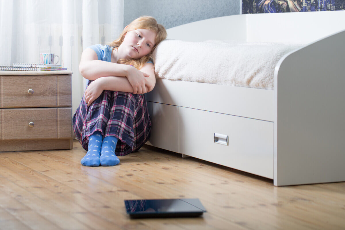 Sad teen girl with scales on floor