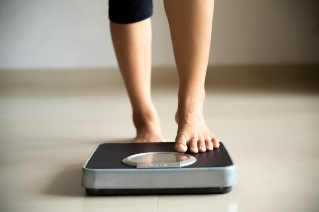 Woman stepping on scale, checking weight loss or weight gain