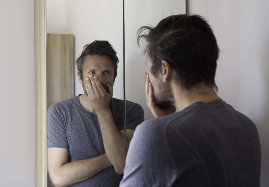 Stressed man looking in mirror