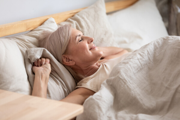 Older woman waking up in bed happy, rested from good night of sleep