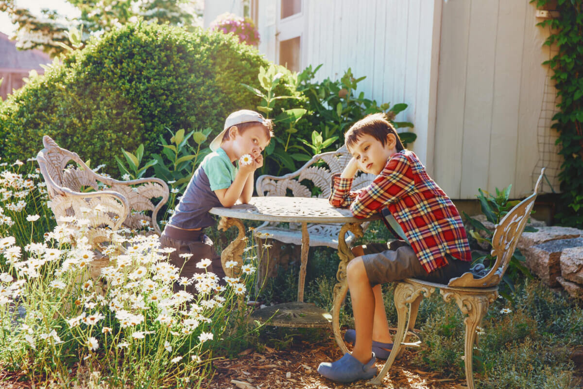 Bored children are sitting in the garden at the table. bored kids in the yard near the house. The concept of idleness and apathy