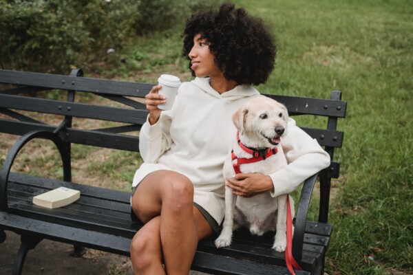 Woman sitting outside on park bench with dog while drinking coffee