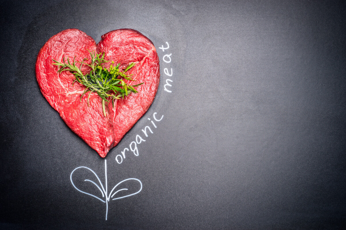 Heart shape raw meat with herbs with painted  Organic meat inscription around . Dark chalkboard background. Healthy lifestyle or organic food concept. For Meat lovers and eater