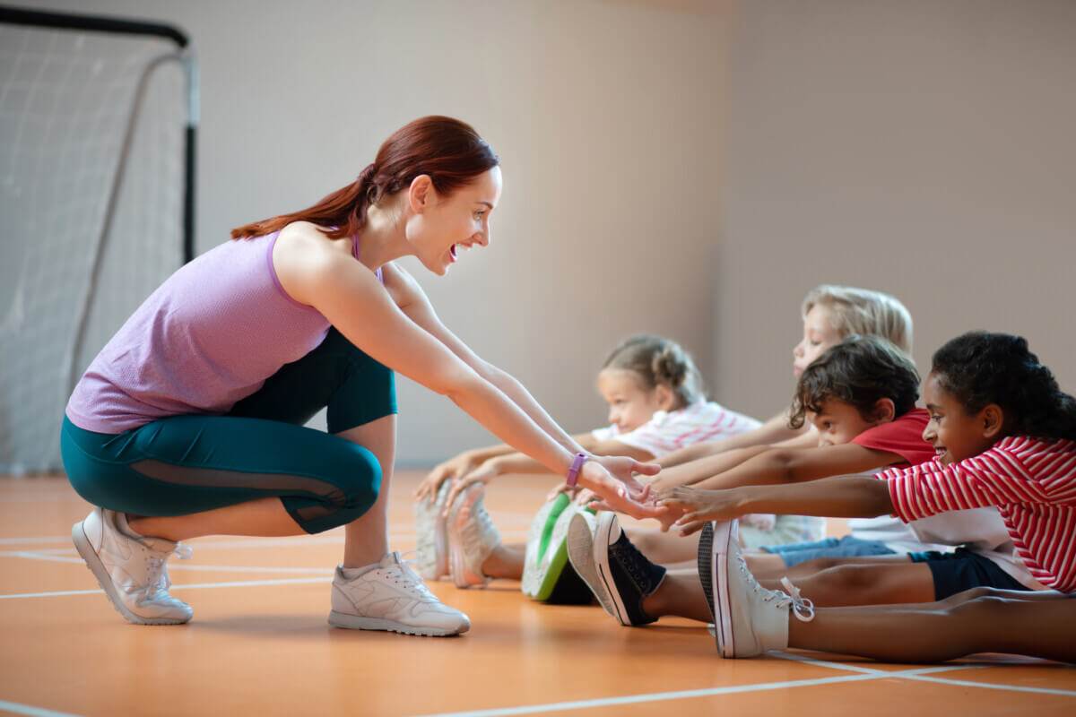 PE teacher smiling while helping girl stretching