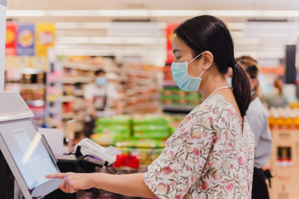 Woman in face mask using self-checkout line at grocery store