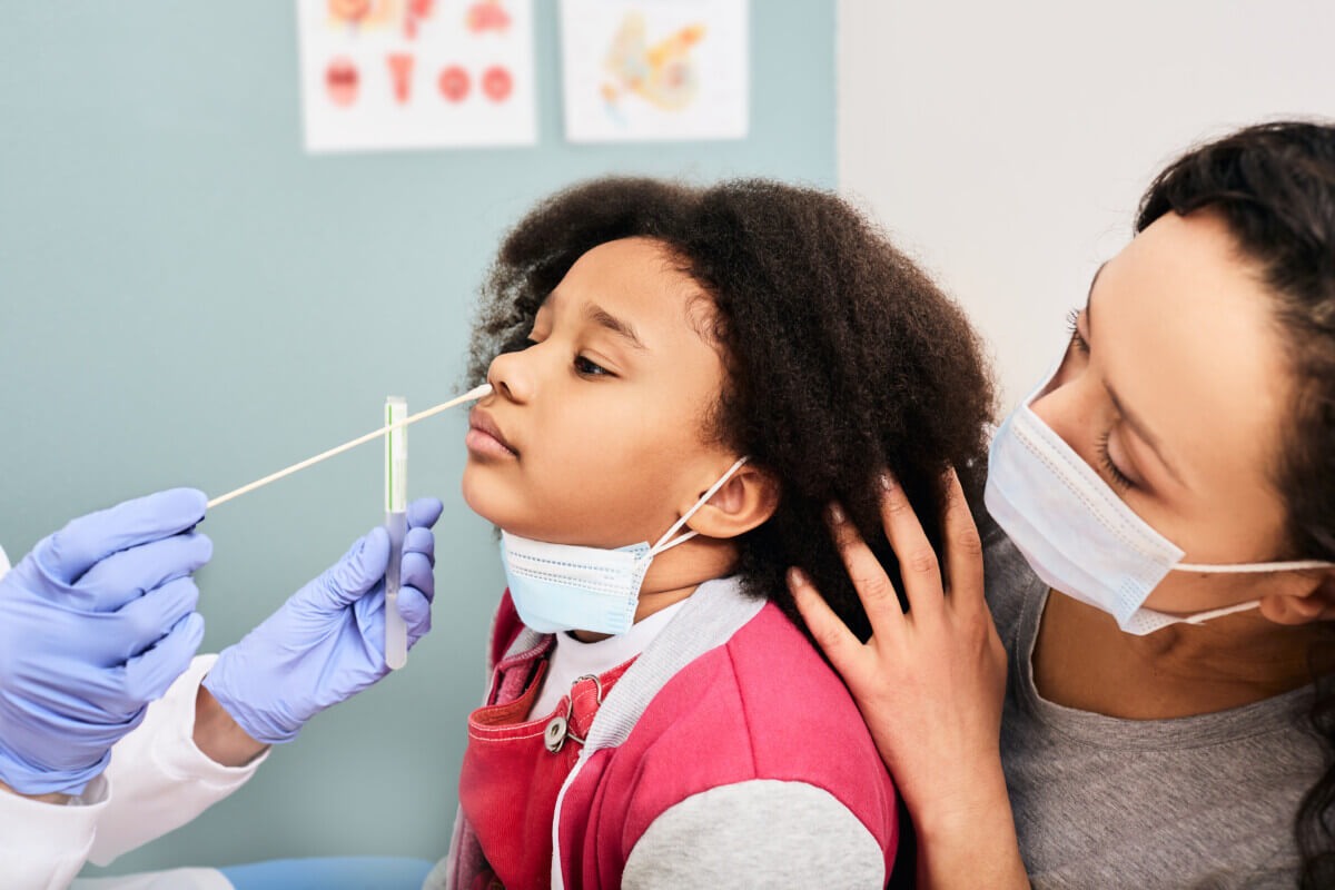 Little girl with her mother during PCR test of COVID-19 in a medical lab. Physician taking a nasal swab for coronavirus sample