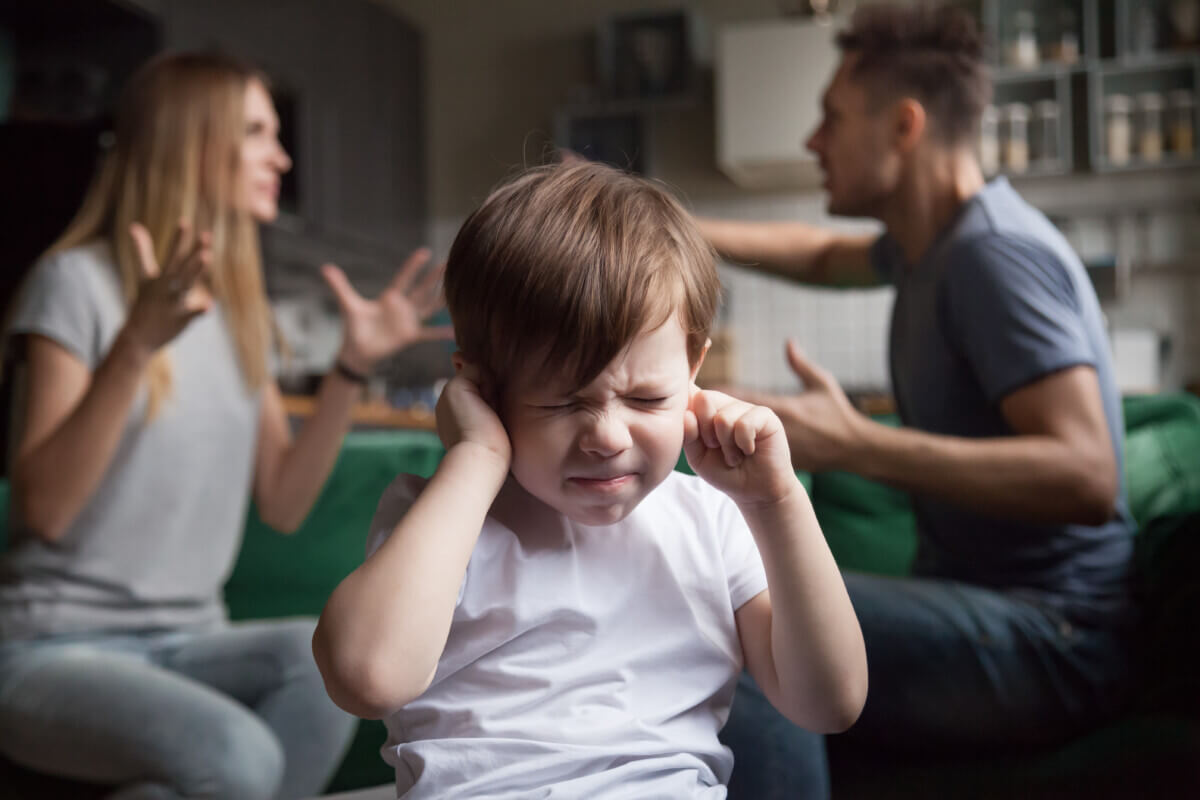 Frustrated child puts fingers in ears while parents arguing