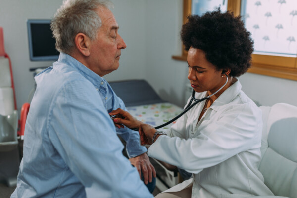 Doctor examining older man, listening to his heart with stethoscope