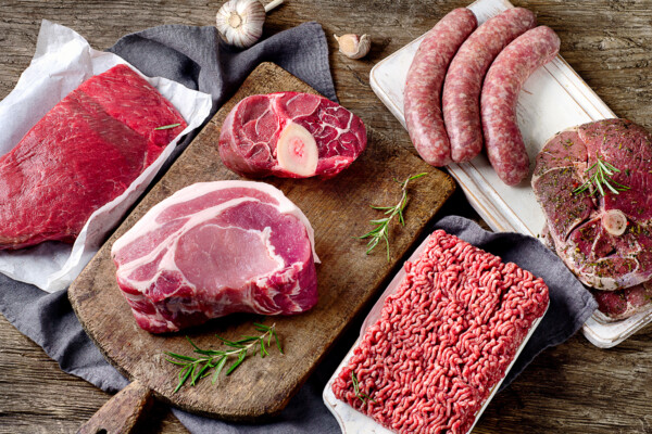 Different types of raw red meat on dark wooden background.