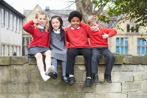 Students in uniforms sitting on wall outside school