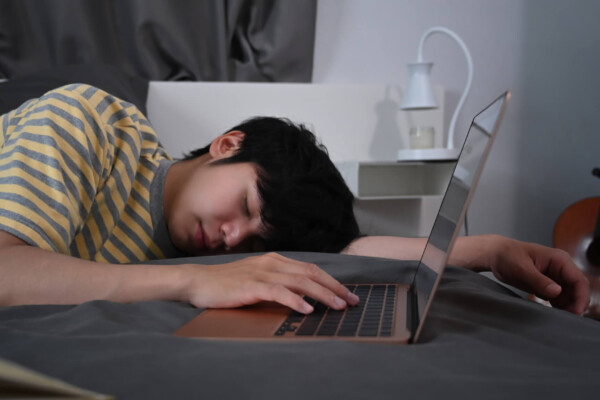 Teen asleep next to laptop computer on bed