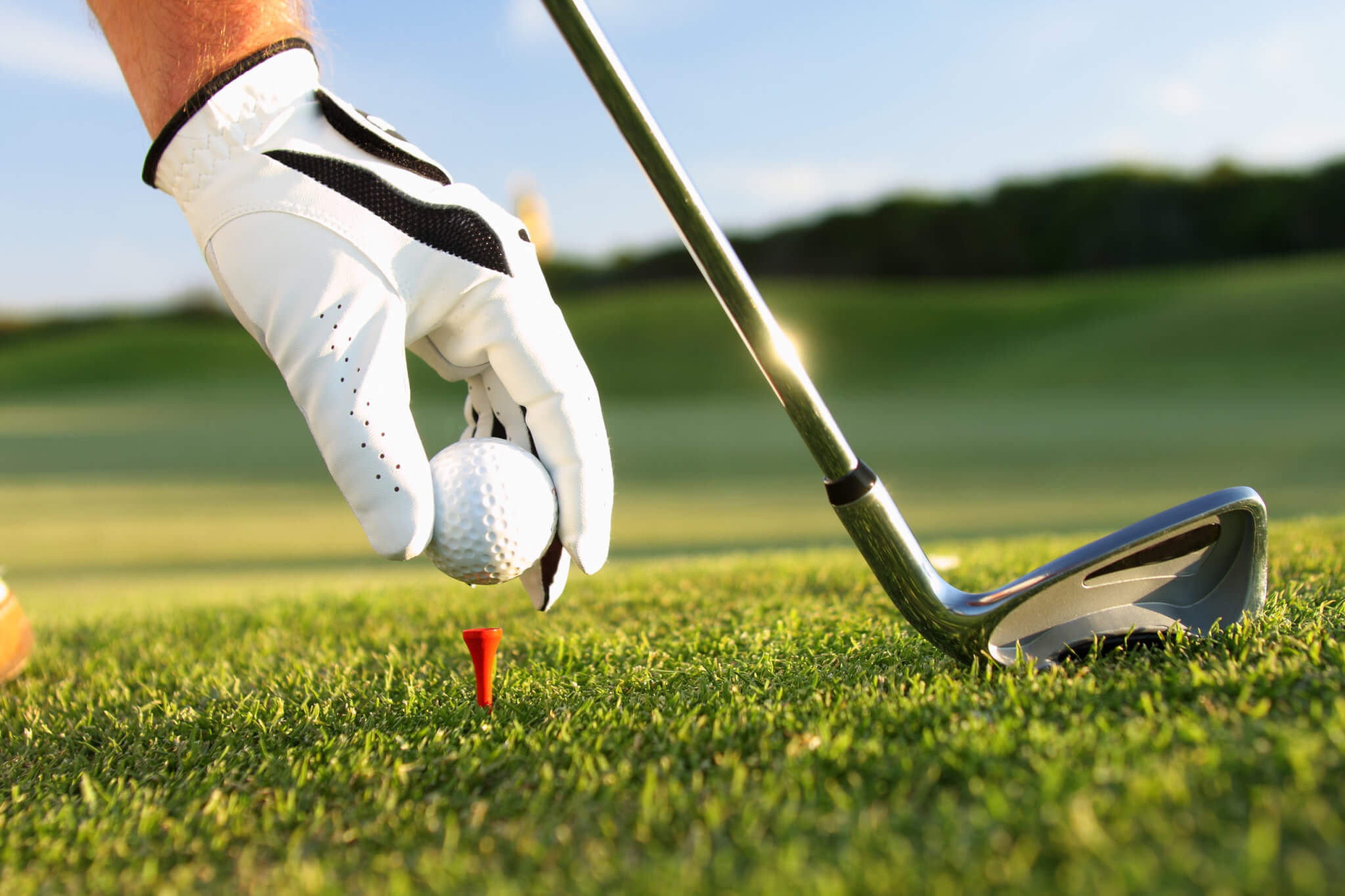 Golfer wearing gloves putting golf ball on tee, holding club