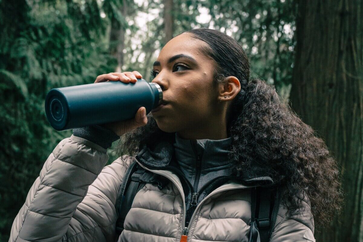 Woman drinking out of a tumbler while walking outside