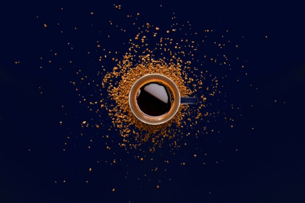 Cup of instant coffee surrounded by grinds