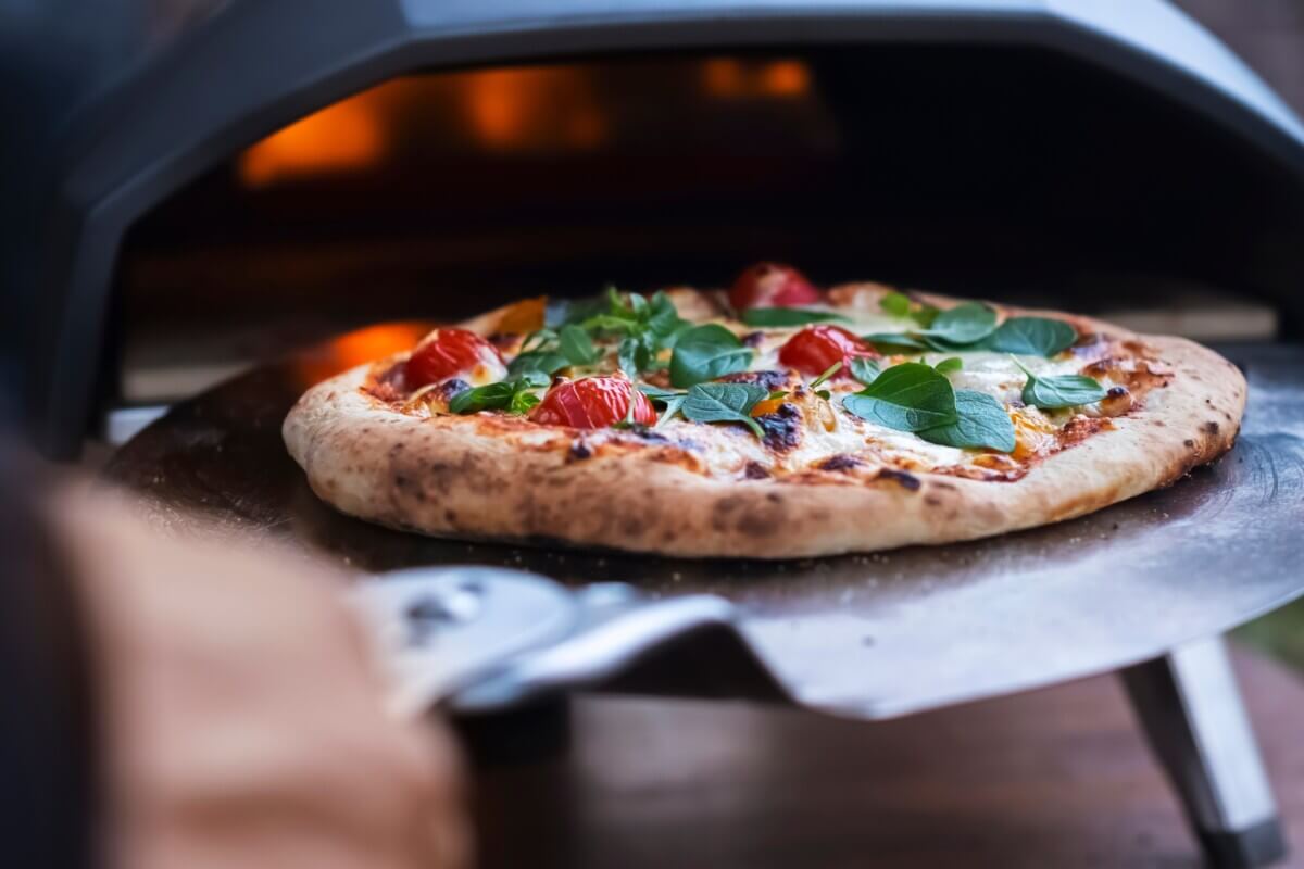 A pizza margarita with fresh basil leaves on the background of a gas oven for cooking pizza